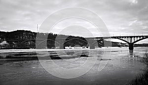 Landscape with a large, multi-span, arched bridge. A black and white photo with a large frozen river and a large bridge over it.