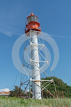 Landscape of lighthouse with red top and white base with green grass and blue sky background. Pape Lighthouse