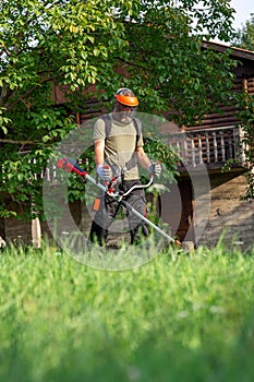 Landscape maintenance concept. Man cutting grass in yard by using electric string grass trimmer