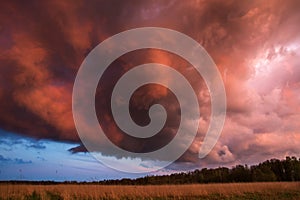 Landscape with majestic colorful dramatic red sky with fluffy clouds at sunset before before a thunderstorm and rain