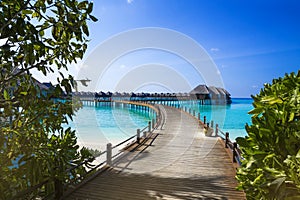 Landscape on Maldives island, luxury water villas resort and wooden pier. Beautiful sky and ocean and beach with palms background