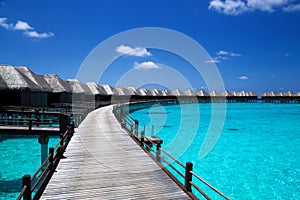 Landscape on Maldives island, luxury water villas resort and wooden pier. Beautiful sky and ocean and beach with palms background