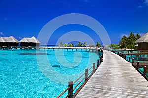 Landscape on Maldives island, luxury water villas resort and wooden pier. Beautiful sky and ocean and beach with palms background