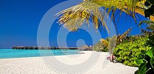 Landscape on Maldives island, luxury water villas resort and wooden pier. Beautiful sky and ocean and beach with palms background