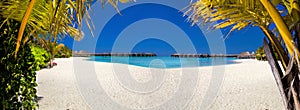 Landscape on Maldives island, luxury water villas resort and wooden pier. Beautiful sky and ocean and beach with palms background