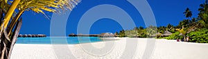 Landscape on Maldives island, luxury water villas resort and wooden pier. Beautiful sky and ocean and beach with palms background