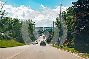 landscape midday view of Canadian Ontario country side road with cars traffic during sunny day with white clouds in blue sky.