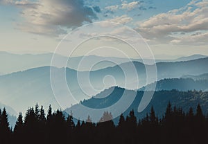 Landscape of misty mountains. View of coniferous forest, layers of mountain and haze in the hills at distance. Beautiful cloudy sk