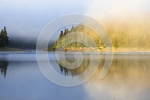 Landscape with mountain forest, fog and lake in morning