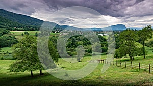 Landscape of mountains, forests, small town, green meadows and two horses