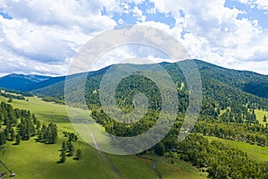 Landscape with mountains, green trees, field, road and river under blue sky and clouds in summer