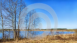 Landscape and nature with calm water of big lake, trees on the shore and blue sky on autumn or spring sunny day. Sun and