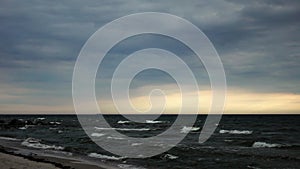 Landscape of ocean next to sand coastline at cloudy weather with waves on water surface in slowmo