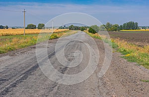 Landscape with an old, cracked asphalt road between fields leading to remote village in Poltavskaya oblast, Ukraine