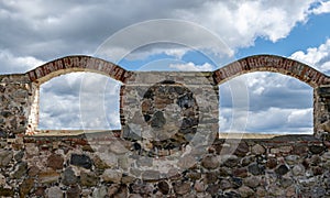 Landscape with an old stone building wall and arched windows, the ruins of a building in a bright green field