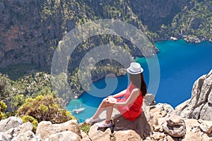 Landscape Oludeniz, Turkey, a young girl in a red dress looks at the Butterfly Valley from above, sitting on the rocks