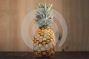 Landscape orientation picture of a Ripe Tropical Pinapple on a wooden table with a wooden background.