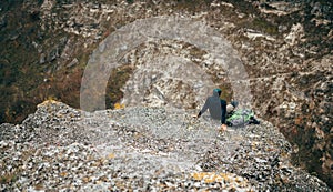 Landscape overhead rear view of hiker man relaxing in mountains after hiking. Outdoors shot of traveler male sitting alone on rock