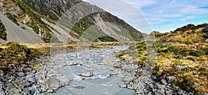 Landscape panorama image of a glacier fed river running through a mountain valley with alpine vegetation