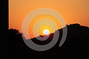 A landscape photo with a bright sun shining brightly from behind a silhouette mountain range and wild silhouette trees.concept to