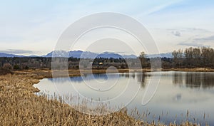 Landscape photo of a pond during fall with blue skies, mountains, and trees as a