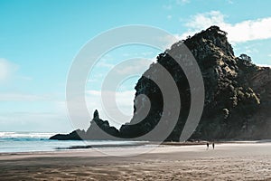 Landscape of the Piha beach and high rocks with the people walking around it under a blue sky