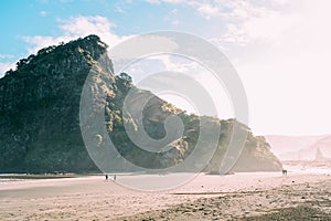 Landscape from the Piha beach with people walking around a high rock under bright sunlight