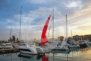 Landscape with red sail at sunset. Fishing boats in harbor. Montenegro, Tivat