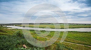 Landscape river in a bright green summer field on a cloudy day