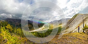 landscape river in a mountain green valley, with thunderclouds and rainbow in the rain on a sunny day