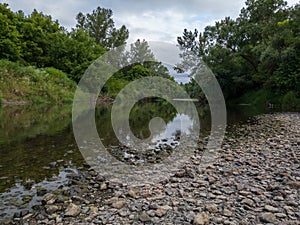 Landscape of river Ukrina with gravel beach and green riparian zone, riverbank overgrown with trees, river ecosystem during