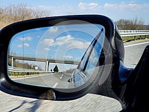 Landscape and road reflection in car rearview black mirror.