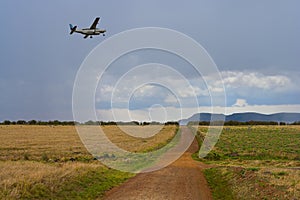 Landscape with a road in the savannah and an airplane in the sky
