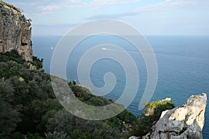 Landscape with rocky mountains with dense vegetation and calm sea far and down on horizon line on sunny day