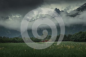 Landscape of Romsdalen with mountains of Troll Wall in rain clouds and red cabin in Norway