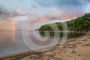 Landscape with sandy beach, dramatic sky, rainy clouds and rainbow.