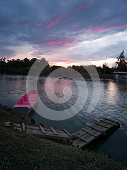 Landscape of Sava river in Bosanski Brod during colorful sunset with wooden dock and moored boat in summer, and pink glow in