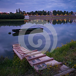 Landscape of the Sava river during a cloudy summer evening, reflection of clouds in calm water, anchored fishing boat near a