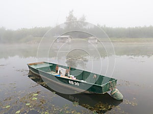 Landscape with Sava river and moored boat in water and fishing huts in fog during foggy autumn morning