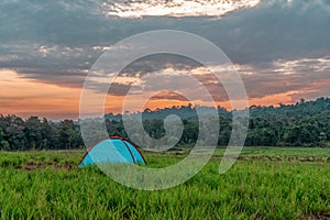 Camping tent on grass field with background of forest and mountains and sunrising sky in natural park