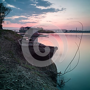 Landscape scenic view of nature of Sava river with old used fishing boat moored along coast to willow stump framed with branch or