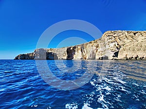 Landscape, sea and rocks on the shore at noon, sea view. A small water cave in a gray rocky shore against the background of the