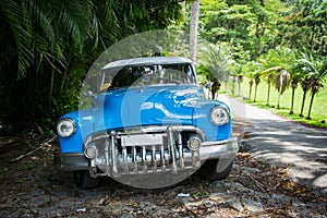 Landscape shot of a blue antique car in a tropical area