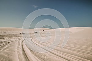 Landscape shot of a desert with tire marks on the sand and motor vehicles in the distance