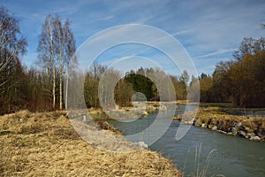 Landscape shot with a small, calm river that flows calmly in the winter against barren trees and dry grass