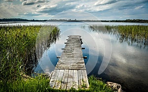 Landscape shot of a weathered wooden dock surrounded by swampy grass leading to a large lake