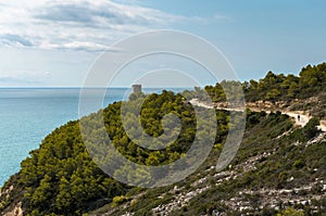 Landscape of Sierra de Irta Natural Park full of green trees with the Badum sentinel tower in the background on a summer day with