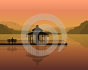 Landscape - silhouette of a man on a bench, and house on the background of the mountains, the sky with reflection in water.