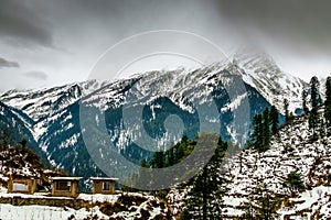 A landscape of a snow capped valley in a mountain with pine trees and houses