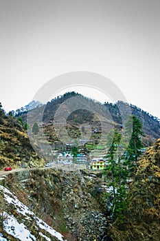 A landscape of a snow capped valley with trees and houses. Mountain with snow capped peaks and blue sky in the background